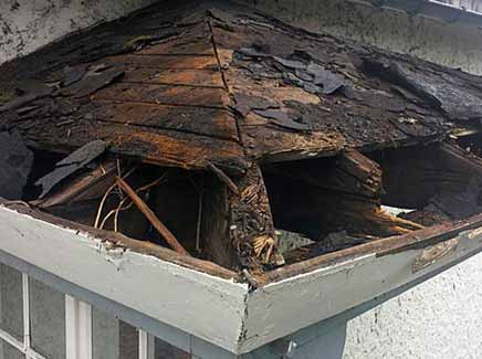 The image shows a damaged roof caused by a storm, with missing or broken shingles, and exposed underlayment. The image is used to illustrate the services of E.W. MacDowell Roofing for repairing storm damage to roofs in West Palm Beach.